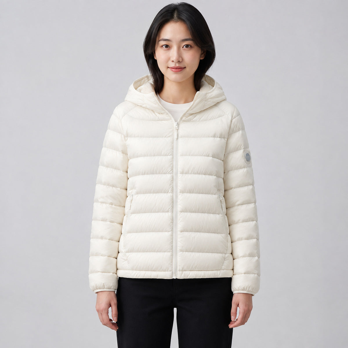 Woman wearing a white quilted nylon hooded puffer jacket with full zip and black pants.