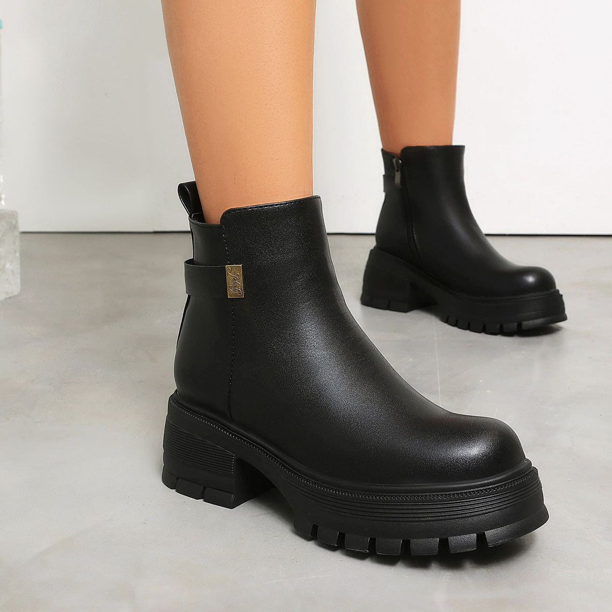 Black faux-leather ankle boots with chunky platform lug soles, side buckle strap, and block heel.