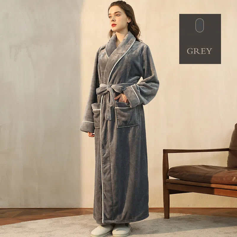 A woman wearing a long, grey plush fleece bathrobe with a shawl collar, white piping, and a tie belt.