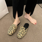 Beige and black leopard print pointed-toe mules with black insoles, worn with black split-hem trousers.