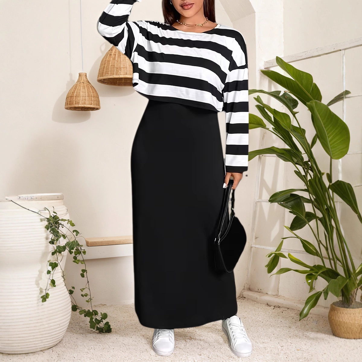 Model wears a black and white striped crop top with long sleeves paired with a long black dress and white sneakers.