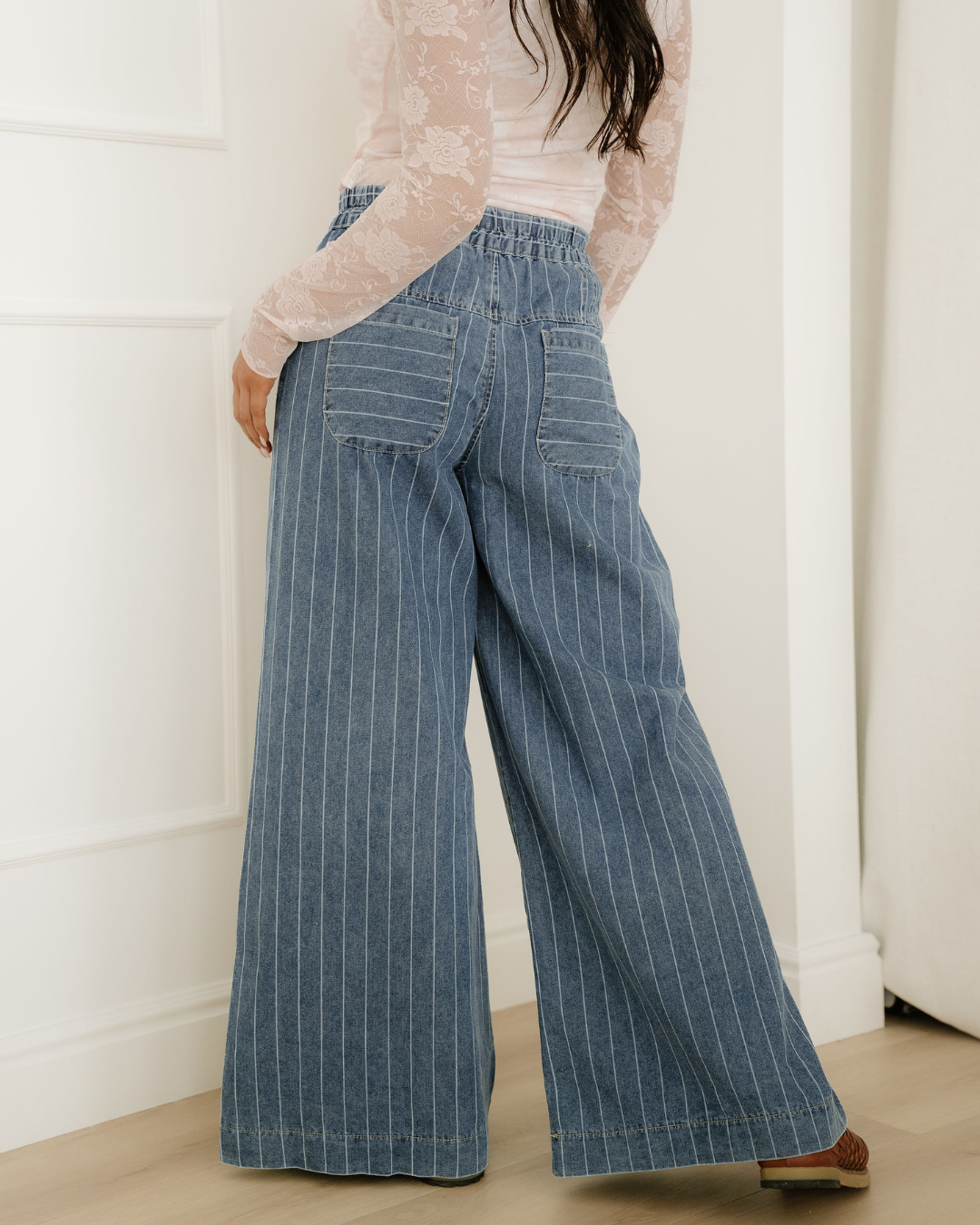 Back view of wide-leg blue denim jeans with white vertical pinstripes and a gathered elastic waistband.
