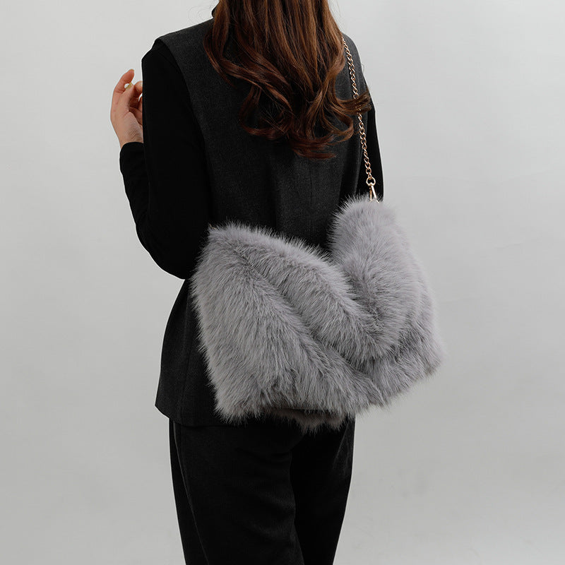 A model wearing a grey faux fur shoulder bag with a gold chain strap.