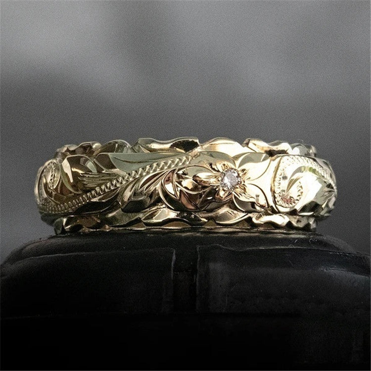Gold band ring featuring intricate floral engraving and a small embedded diamond, with scalloped edges.