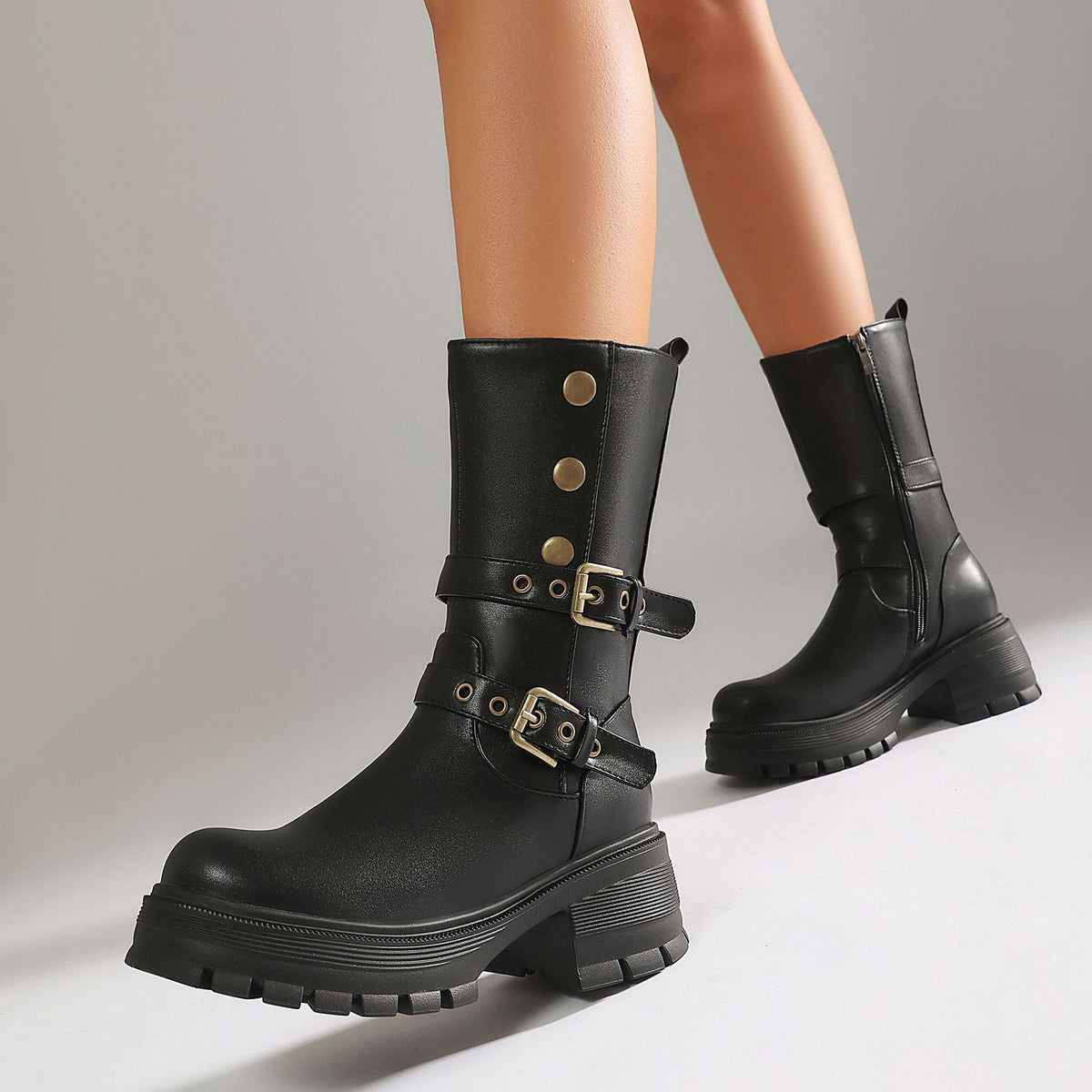 Black faux leather mid-calf boots, featuring two buckle straps, grommets, and chunky lug soles.