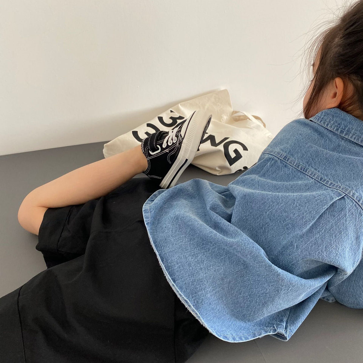 Black canvas sneakers with white laces and soles worn with black shorts and a denim shirt.