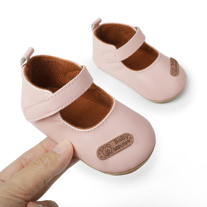 Pair of pink leather baby Mary Janes with brown corduroy lining and a strap, featuring a bear patch.