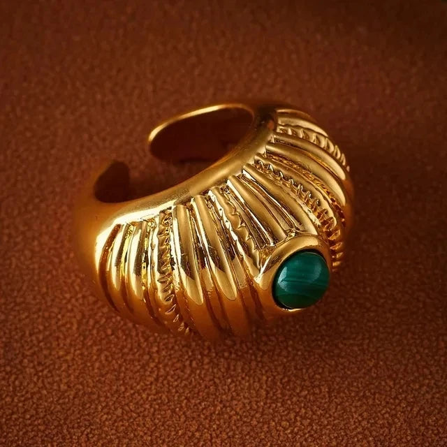 A chunky gold metal ring with vertical ridges and a central green gemstone.