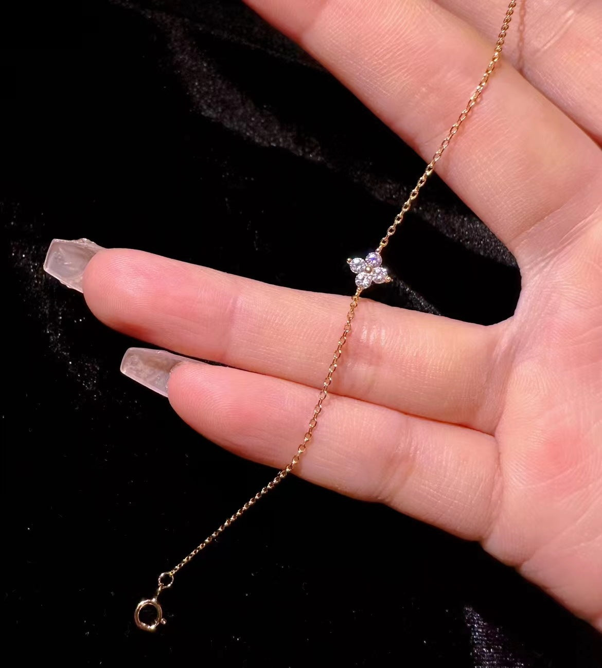 Gold chain bracelet featuring a four-petal flower charm set with small sparkling clear stones.
