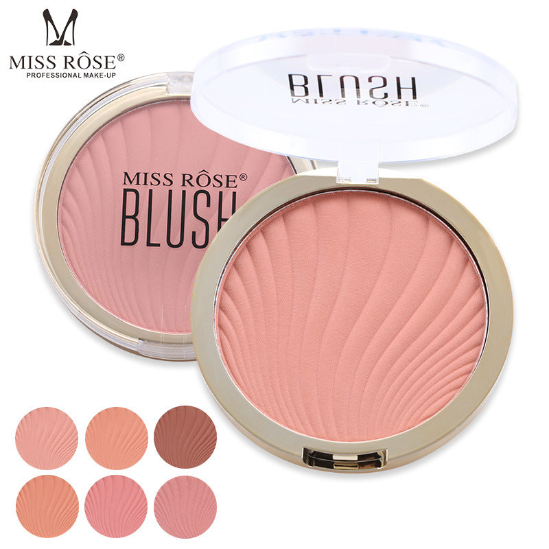 Miss Rose peach blush in a round gold case with clear lid, featuring a swirled powder texture and six color swatches.