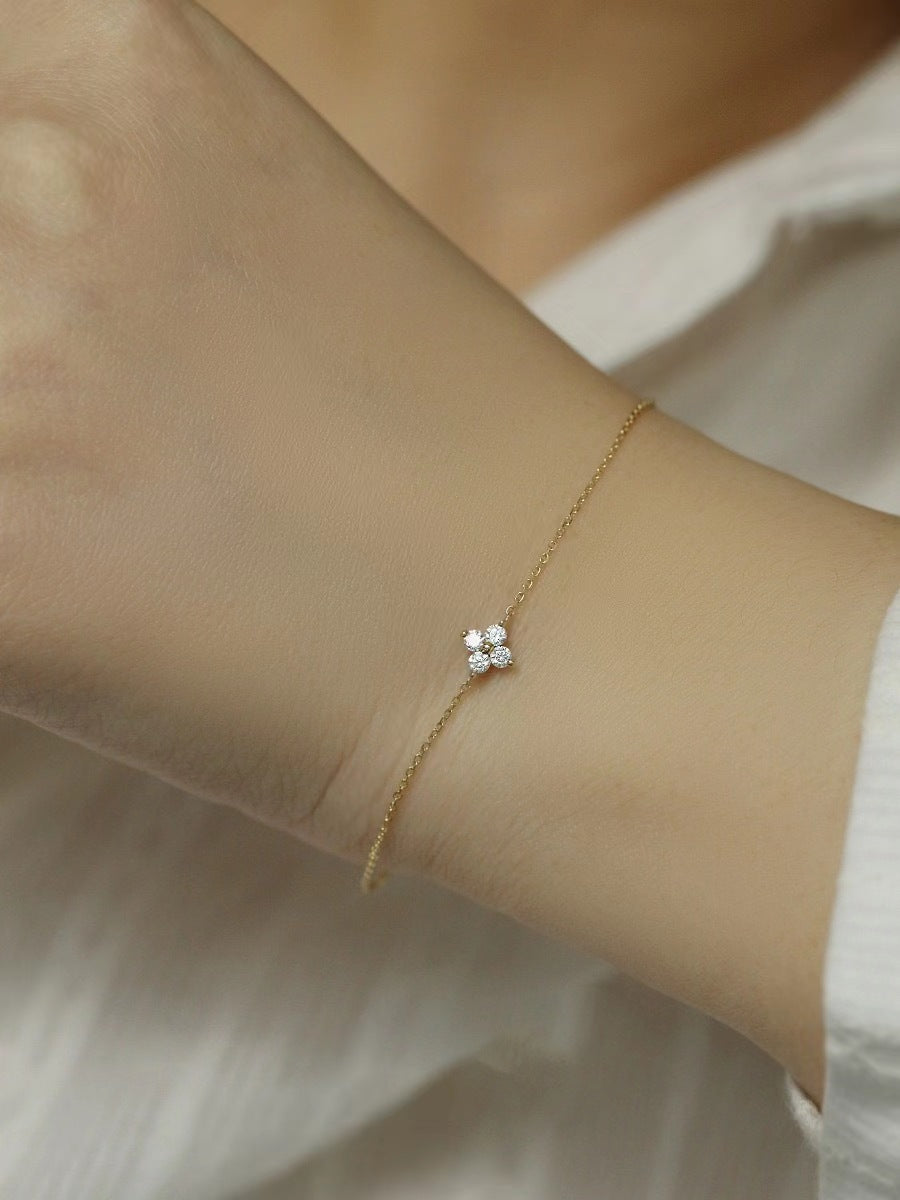 A delicate gold chain bracelet on a wrist features a four-stone diamond clover charm.