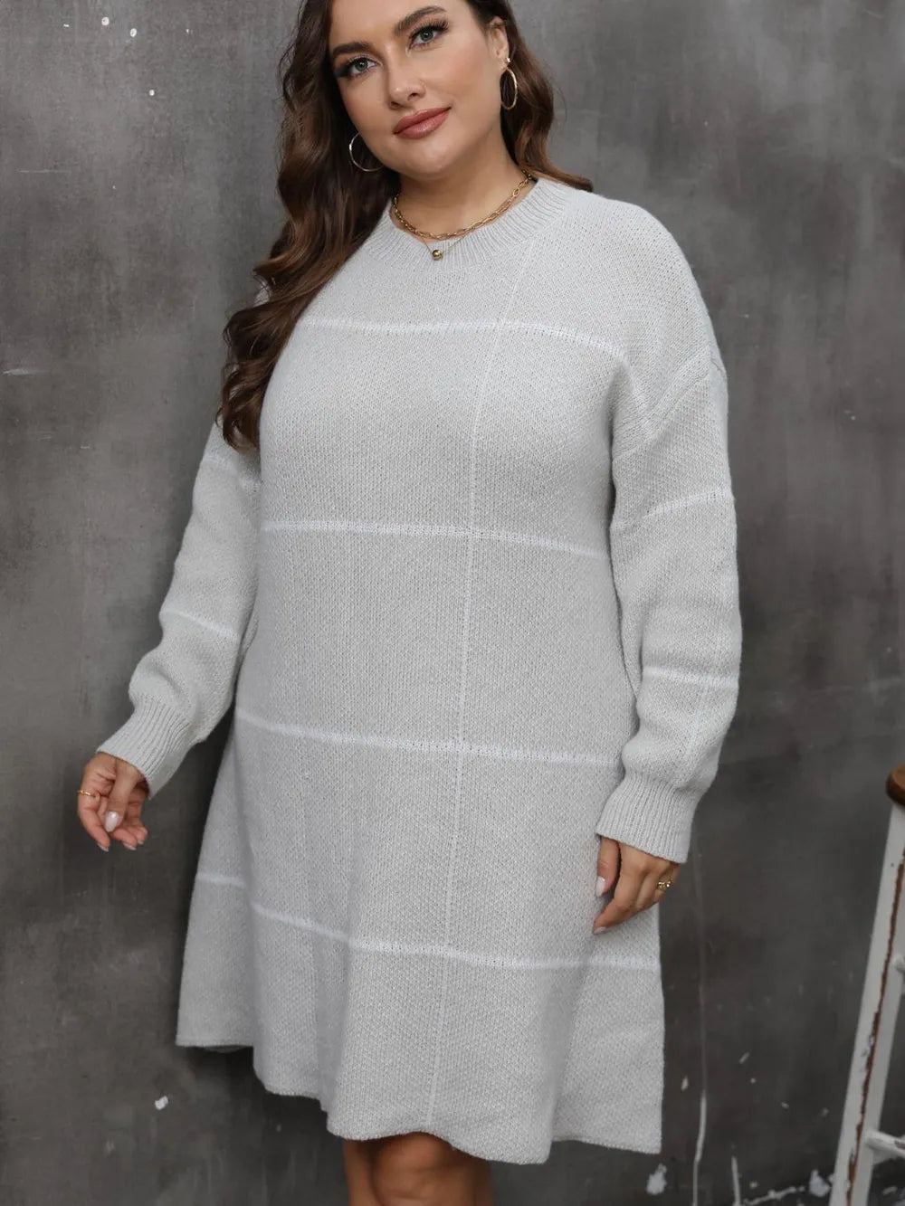 A plus-size model wears a grey knit long-sleeve sweater dress with a subtle plaid pattern and round neckline.