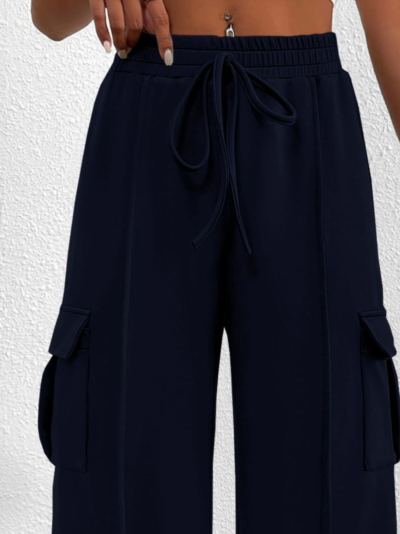 Women's high-waisted casual cargo pants with drawstring, lightweight utility style, shown in neutral color with multiple pockets.