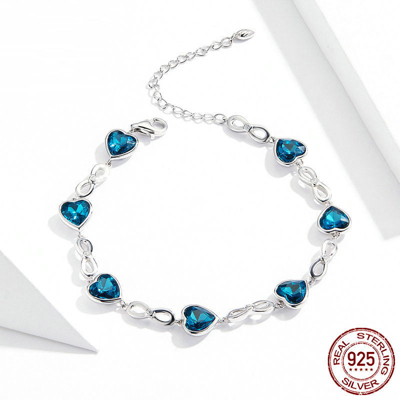 A silver bracelet with alternating blue heart-shaped gems and infinity symbols.
