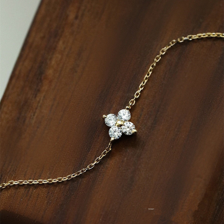 Delicate gold chain bracelet featuring a four-stone cubic zirconia flower pendant on dark wood.