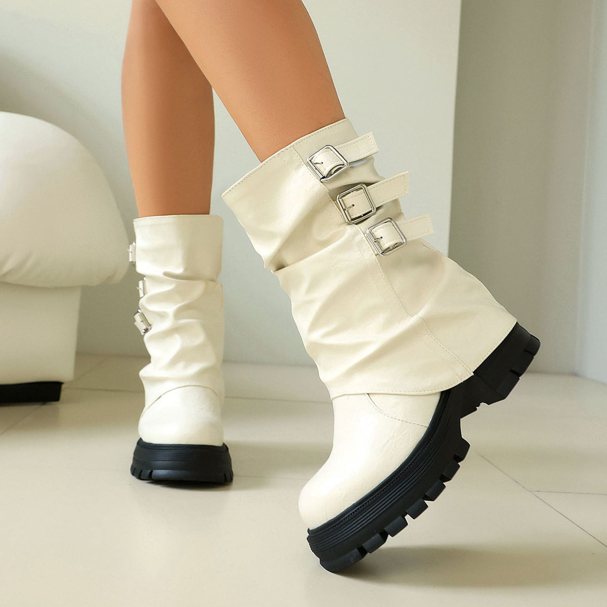White faux leather slouchy mid-calf boots with three side buckles and black platform lug soles.