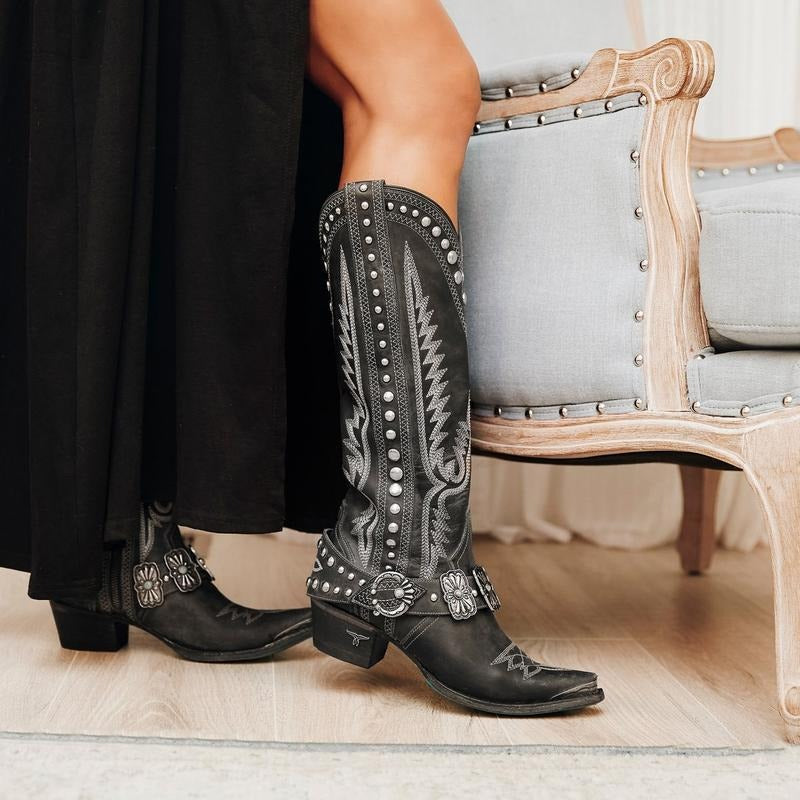 Black leather western boots with white stitching, silver studs, and concho harness straps.