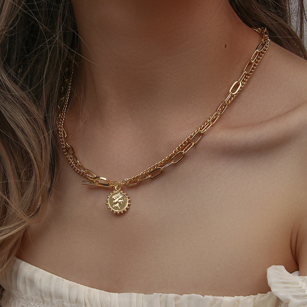 Layered gold metal chain necklace with a coin pendant featuring a profile portrait and toggle clasp.