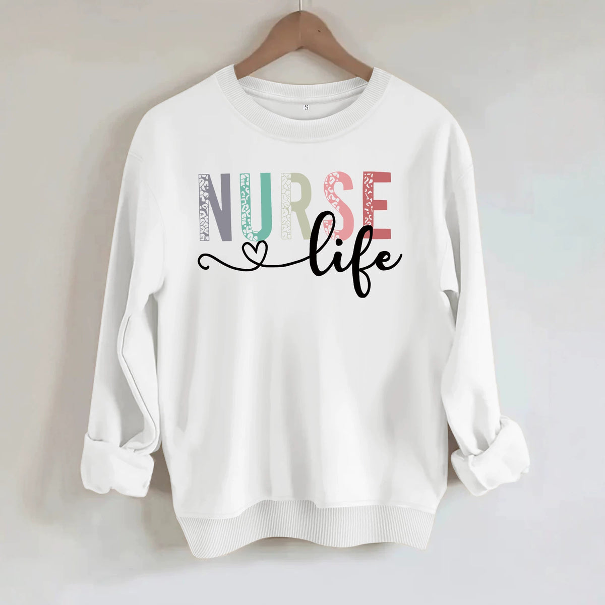 White cotton sweatshirt with "NURSE life" graphic; letters feature pastel leopard print and black script with heart.