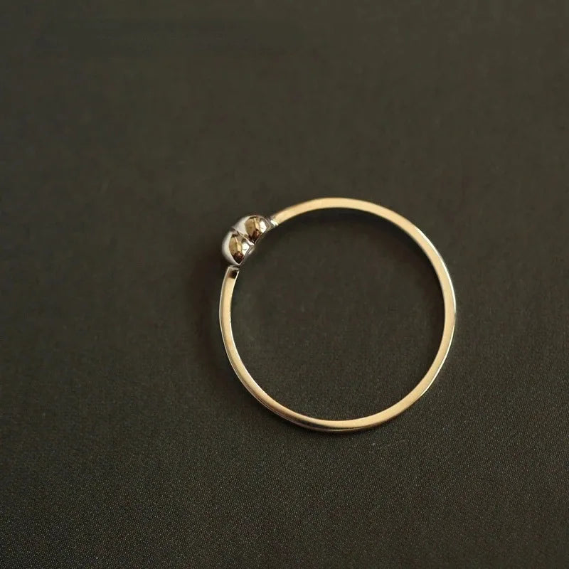 Minimalist silver ring with a thin band and two tiny beads at the open end, set against a dark background.