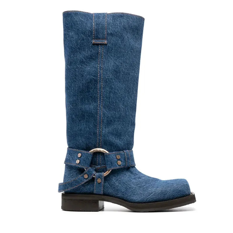 A blue denim knee-high boot with a square toe, harness strap, and low heel, shown in profile.