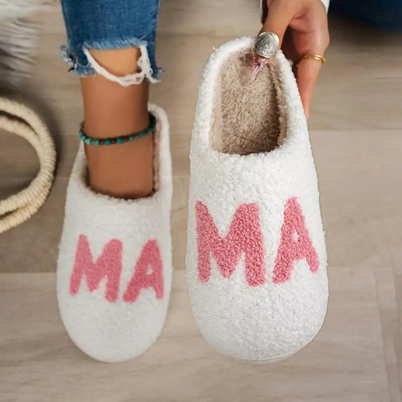White fuzzy fleece slip-on slippers with pink chenille "MAMA" lettering on top.