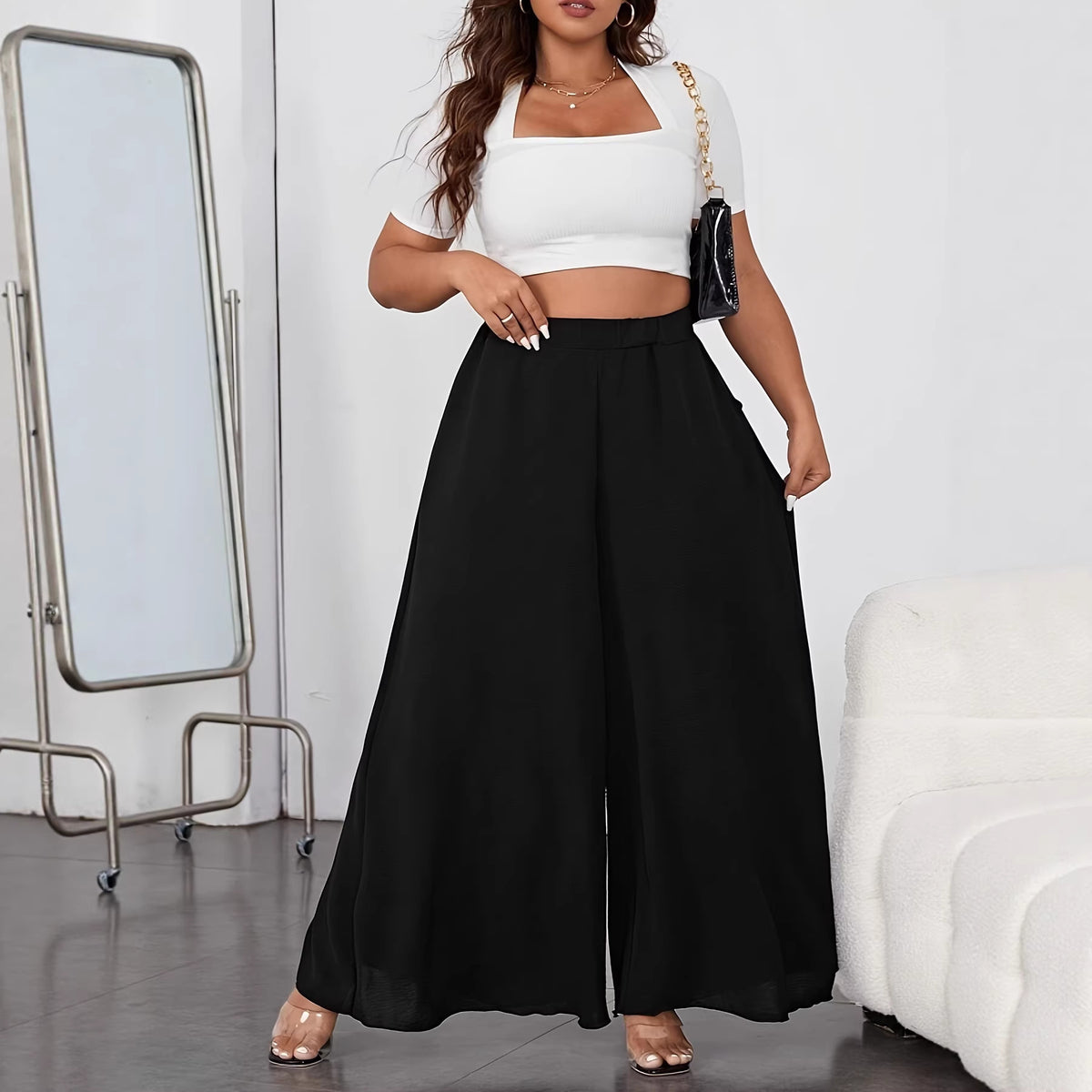 A woman wearing solid black, high-waisted, wide-leg chiffon pants with a white crop top.