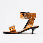 Eprolo rivet accent mid-heel strappy sandals showing sleek straps and stylish rivet details on a beige background.
