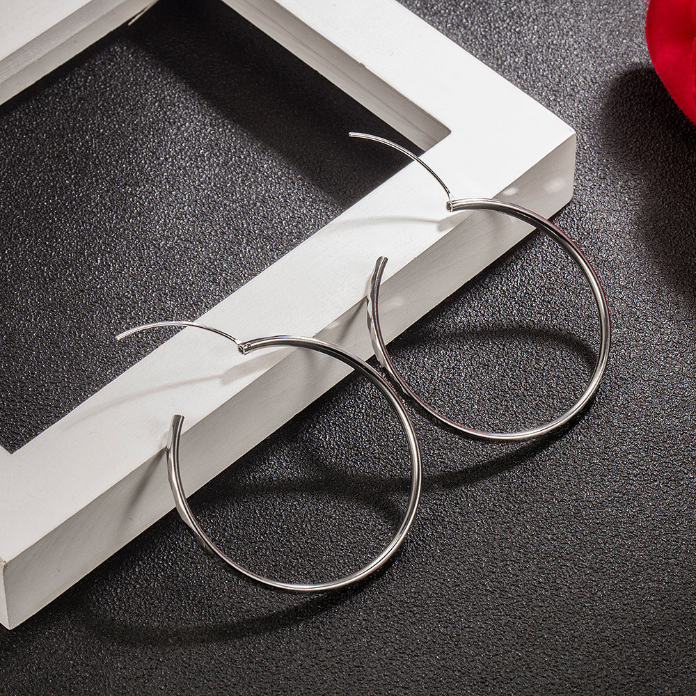 Silver hoop earrings with a thin wire closure, resting on a textured dark surface beside a white frame.