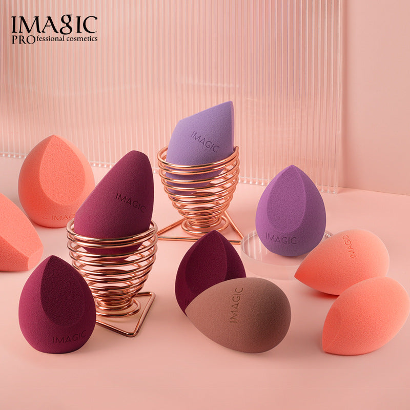 Tear-drop shaped foam makeup sponges in pink, purple, and brown, with two in rose gold wire stands.