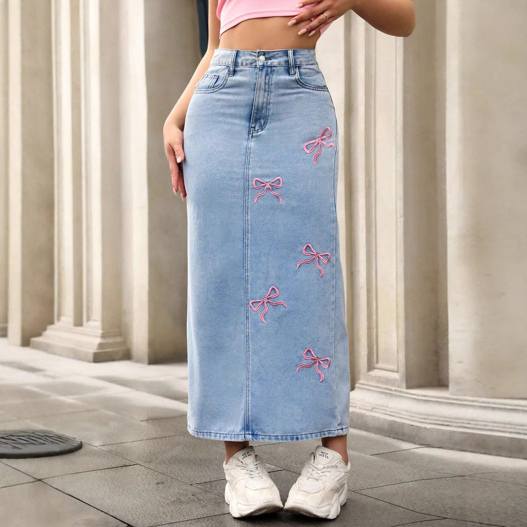 Light blue denim maxi skirt featuring embroidered pink bow patterns, high waist, and straight fit.