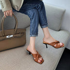 Tan square-toe stiletto mule heels with quilted crisscross straps, worn with cuffed jeans and a matching handbag.