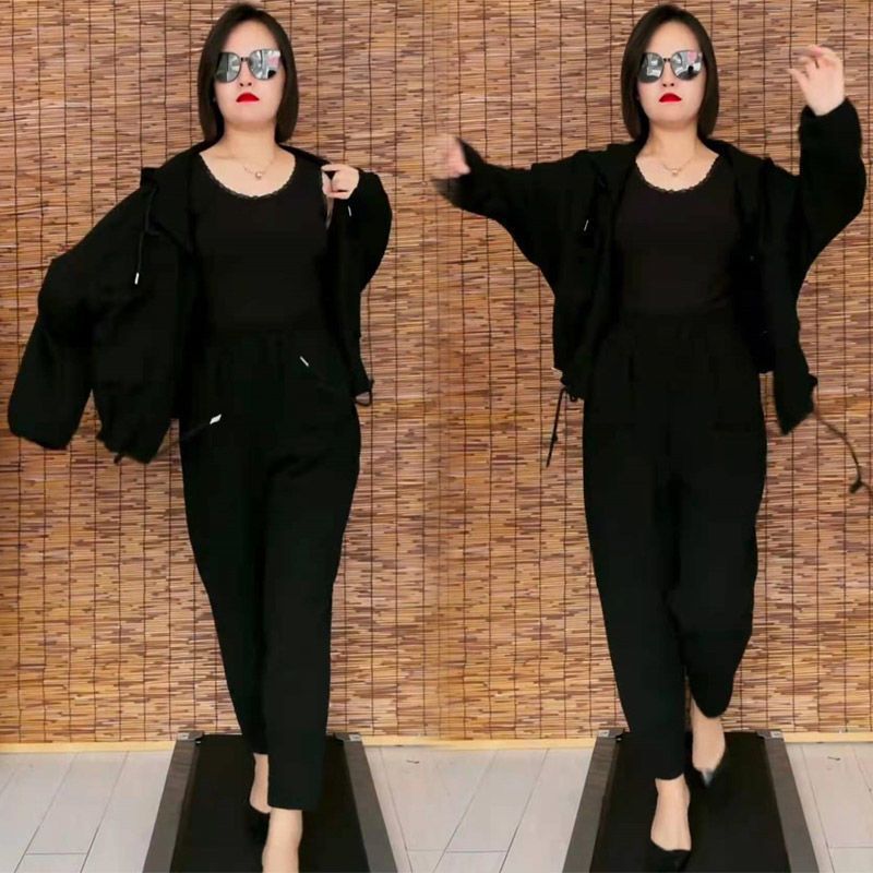 A person wears a solid black cotton tracksuit, including a hooded jacket and pants, with a matching black tank top.
