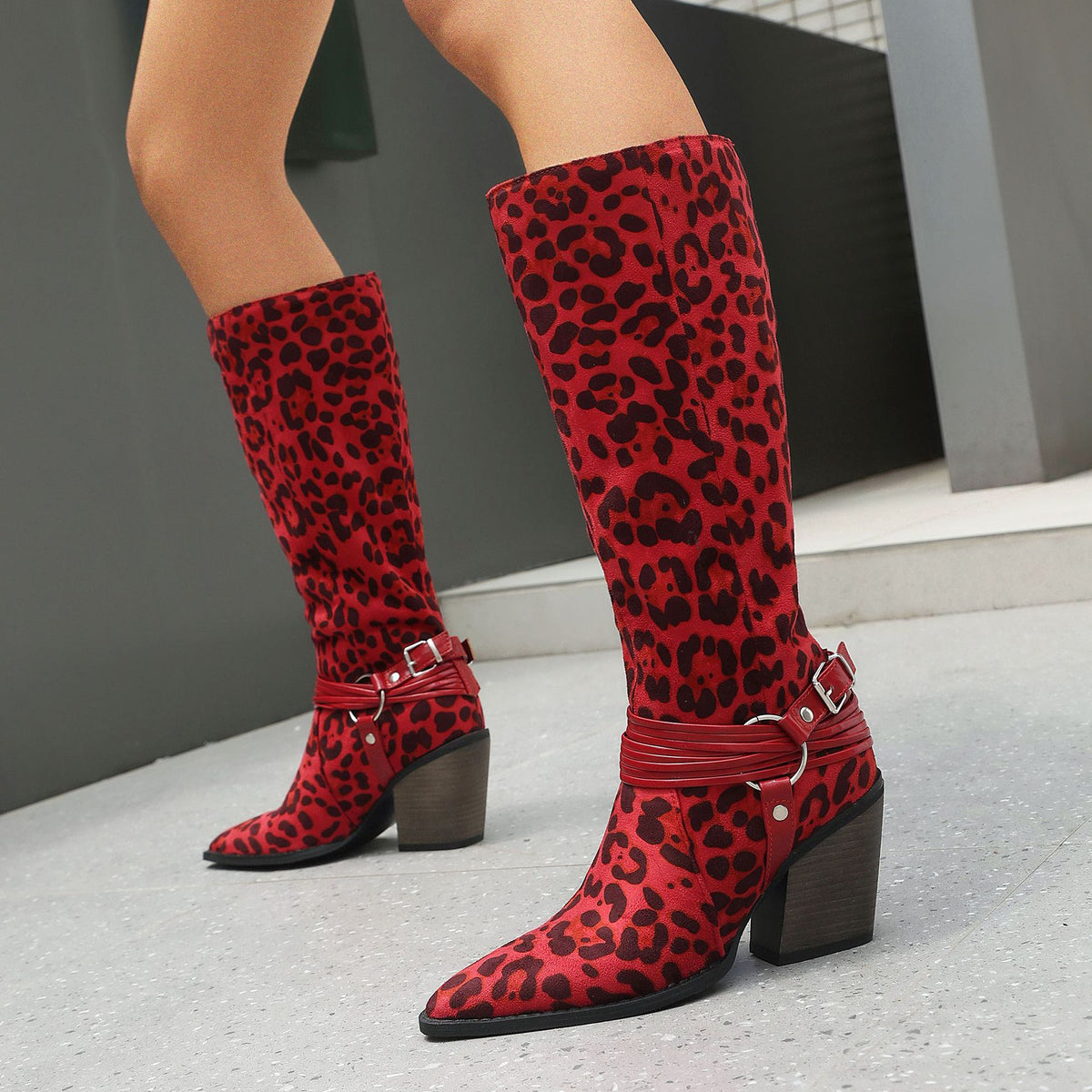 Red leopard print faux suede knee-high boots with pointed toes, block heels, and buckled strap harness details.
