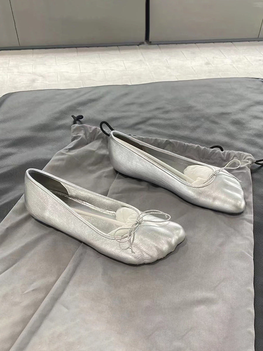 Metallic silver leather ballet flats with a rounded toe, subtle gathered texture, and a delicate tie bow on top.