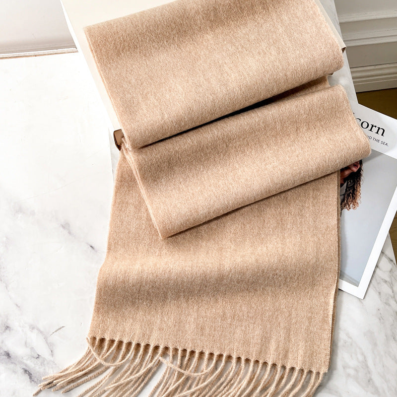 Beige cashmere scarf with fringed ends, neatly folded on a white surface.