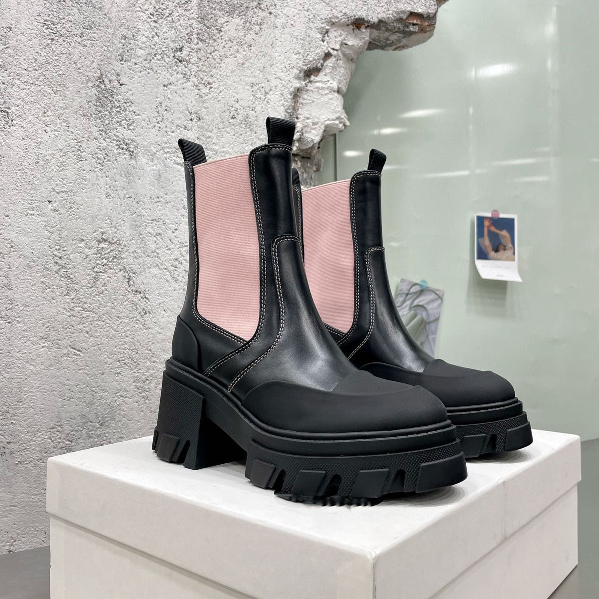 Black leather Chelsea boots with chunky lug heels and soles, featuring light pink elastic side panels and white topstitching.