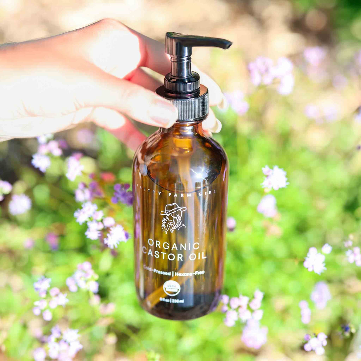 Pure organic cold pressed hexane-free castor oil bottle from Pretty Farm Girl, shown outdoors against a natural background.