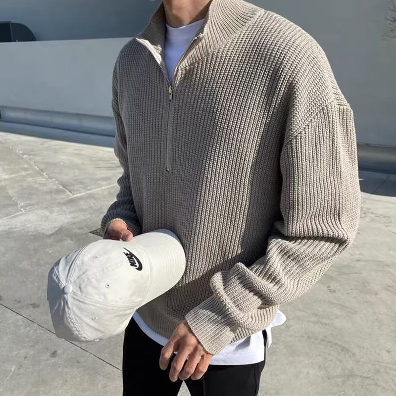 Beige ribbed-knit quarter-zip sweater with high collar, long sleeves, and a relaxed fit, worn over white and black.