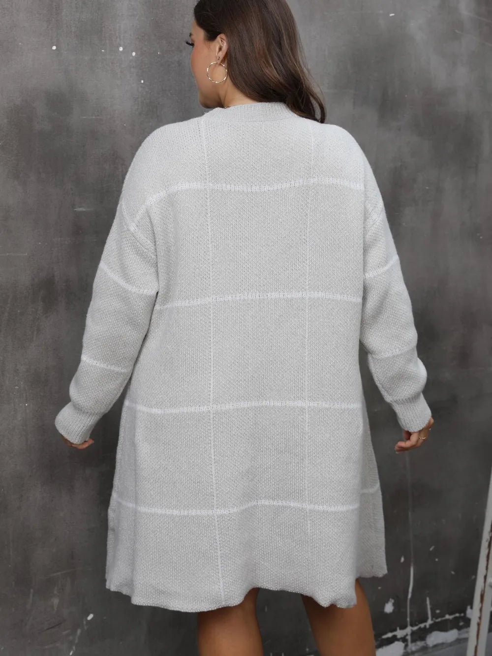 A back view of a person wearing a light gray knitted long-sleeve sweater dress with a subtle plaid pattern.