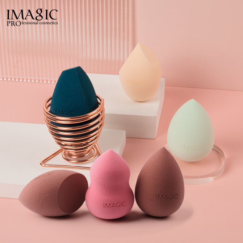 Five makeup sponges in teal, peach, mint, pink, and brown, with IMAGIC logos, displayed with a rose gold holder.