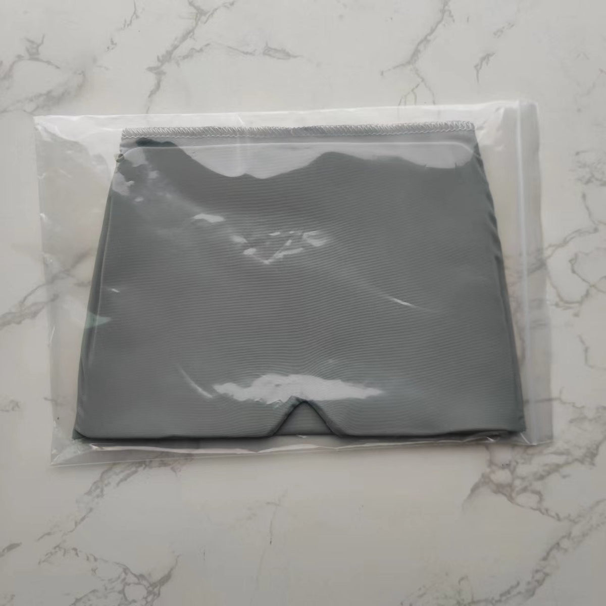 Gray solid-pattern shorts in plastic packaging on a marble surface.