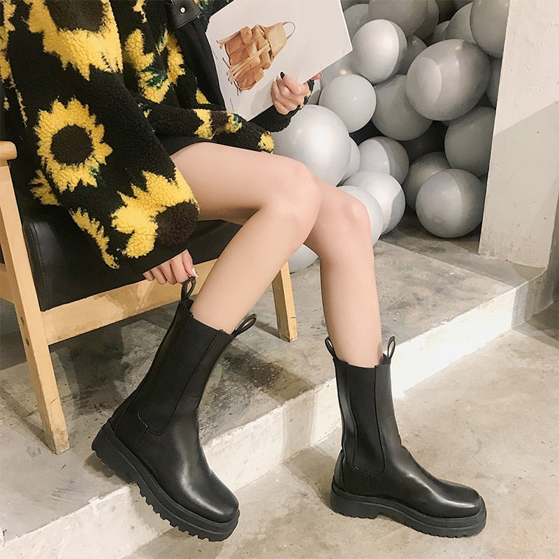 Black faux leather mid-calf platform boots with pull tabs and elastic side panels worn with a sunflower jacket.