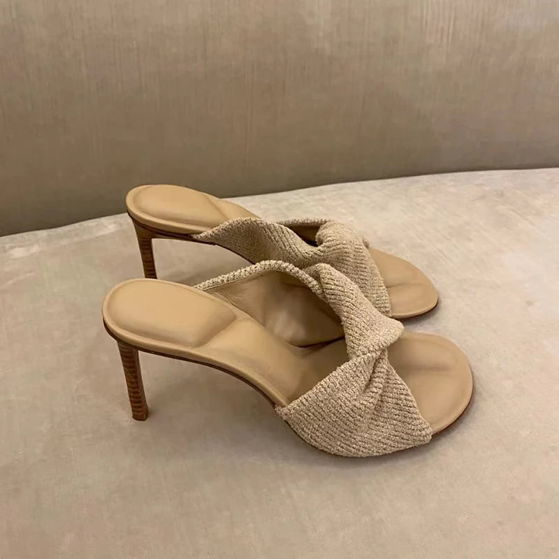 Beige stiletto slide sandals with a textured, knot-accented knit strap and wooden-effect heel.