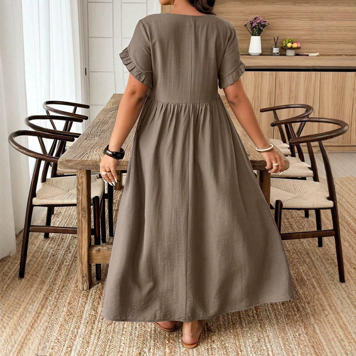 Back view of a taupe maxi dress in a solid, textured cotton fabric, featuring short ruffled sleeves and an empire waist.