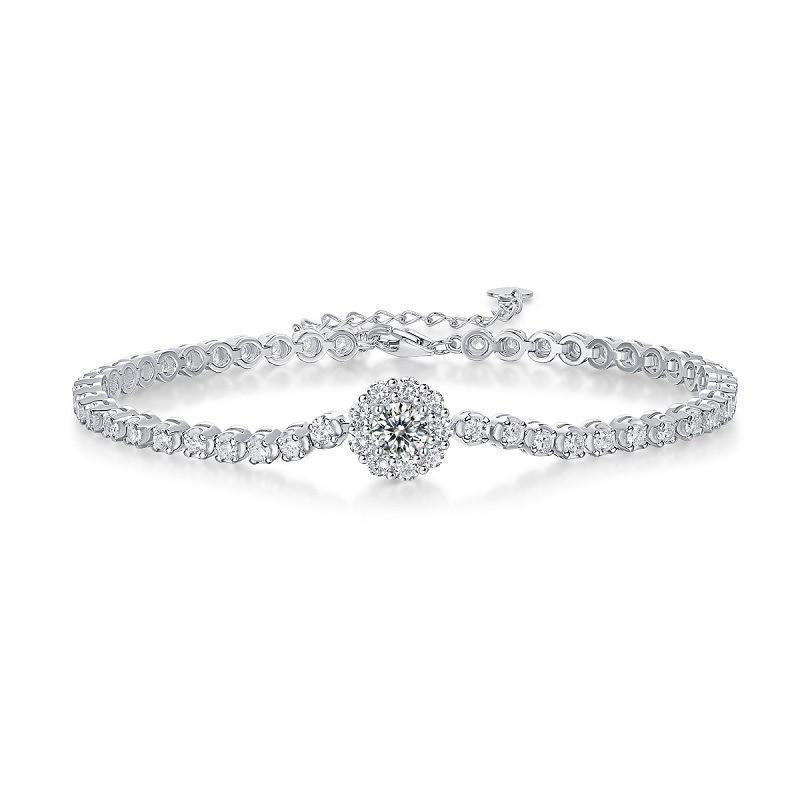 A silver tennis bracelet with a circular cluster pendant set with clear stones on a white background.