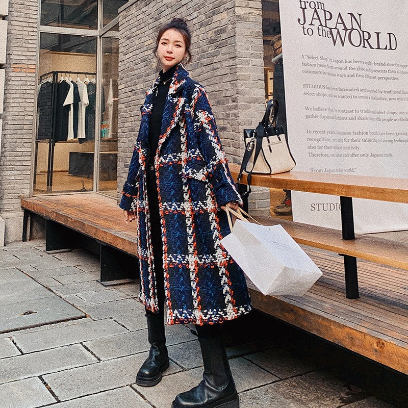 A woman wears a mid-length blue, white, and orange plaid woolen overcoat outdoors.