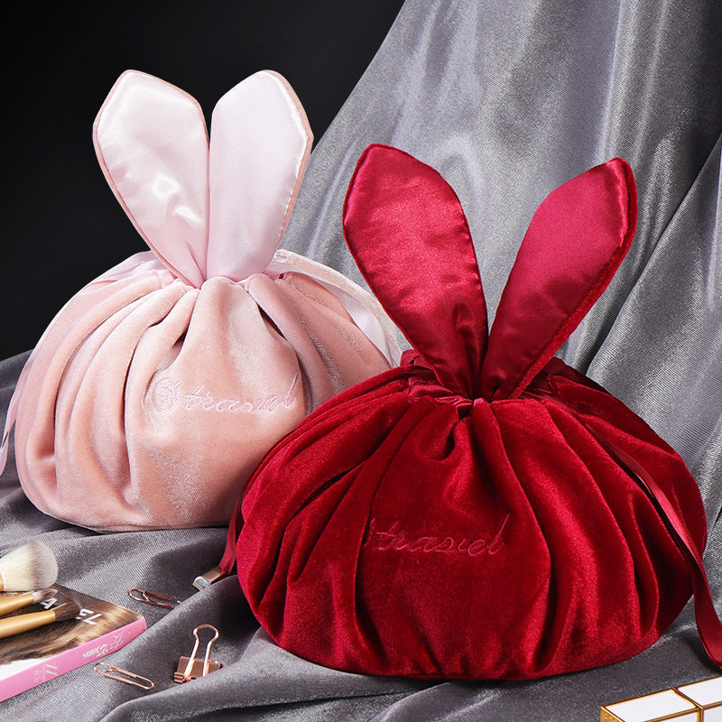 Two velvet makeup bags with rabbit ears, in pink and red, featuring embroidered text and gathered drawstring style.