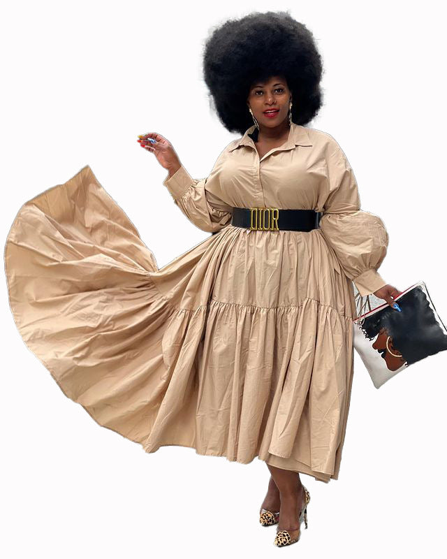 Model wearing a solid tan, long-sleeved midi shirt dress with a tiered skirt, belted at the waist with a thick black belt.