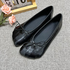 Sophisticated black glossy slip-on flats with round toes and decorative front bows on a grey textured background.